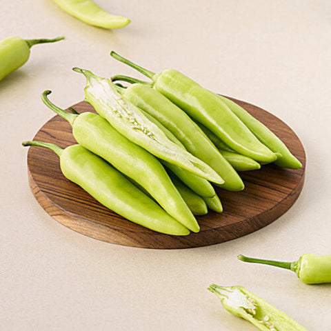 Green chili peppers on a wooden cutting board with a beige background